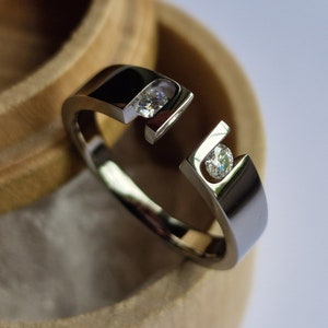 Op de afbeelding: Een zilveren ring met twee kleine diamanten die in de band zijn gezet. De ring ligt in een houten doos.