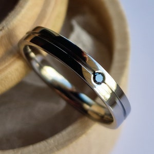 Op de afbeelding: Een zilveren trouwring met een enkele zwarte diamant in het midden. De ring ligt in een houten doos.