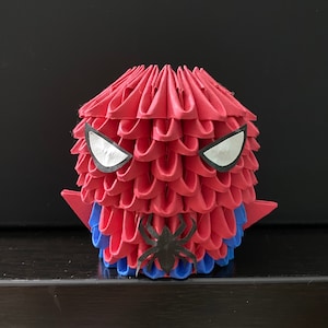 Może przedstawiać: Czerwona i niebieska figurka origami Spider-Mana z białymi oczami i czarnym wzorem pająka.