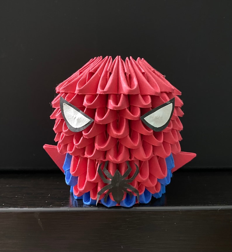 Może przedstawiać: Czerwona i niebieska figurka origami Spider-Mana z białymi oczami i czarnym wzorem pająka.