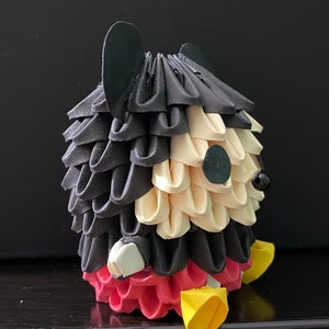 May include: An origami Mickey Mouse figure made from black, white and red paper. The figure is folded into a three-dimensional shape.