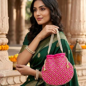 May include: A bright pink drawstring pouch bag featuring an intricate gold and white star-patterned embroidery. The bag is equipped with a handle made of multiple strands of small white pearls and includes gold-toned metal accents at the drawstring ends.