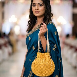 May include: A round yellow drawstring pouch bag featuring a repeating white floral embroidery pattern and a beaded handle made of multiple strands of small white pearls. The bag has a cinched top closure with matching yellow fabric drawstrings.