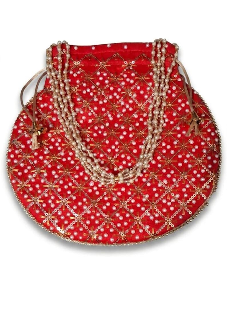 May include: A round red drawstring pouch featuring a gold-toned lattice pattern with embedded white faux pearls. The bag is adorned with a decorative handle made of multiple strands of white faux pearls and includes thin side drawstrings.