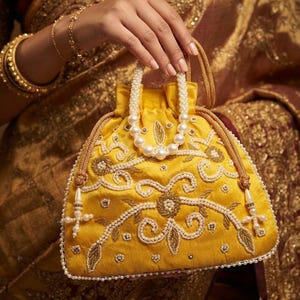 May include: A bright yellow drawstring handbag featuring intricate gold thread embroidery and white pearl bead embellishments. The bag has a structured base, a pearl-beaded top handle, and gold cord drawstrings with dangling pearl accents.