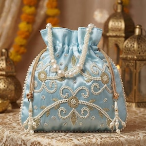 Peut inclure: Un sac bourse bleu clair à cordon de serrage, orné de broderies complexes en perles blanches et fil doré. Le sac possède une anse en perles et deux pompons latéraux avec des perles. La surface présente des motifs floraux et une bordure perlée.
