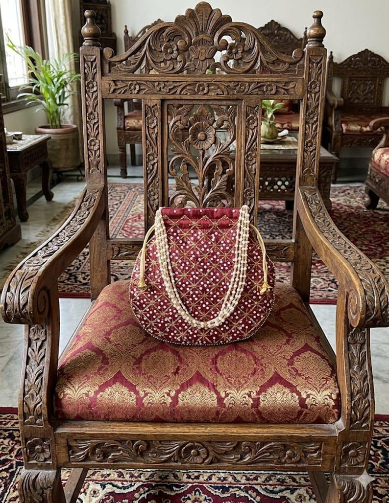 May include: A deep red drawstring pouch featuring a repeating gold embroidered star pattern with small white beads at each intersection. The bag includes a double-strand white pearl handle and gold-toned drawstrings, creating a structured circular shape.