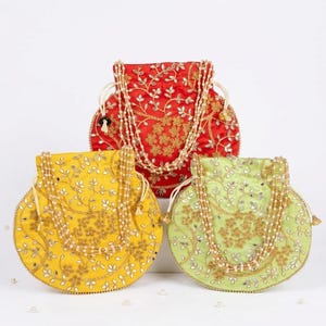May include: Three round drawstring pouches in red, yellow, and light green. Each pouch features intricate gold embroidery, small reflective mirror accents, and a decorative handle made of multiple strands of small white beads for carrying.