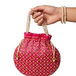 May include: A vibrant hot pink drawstring pouch bag featuring an intricate gold embroidered star pattern and scattered white faux pearls. The bag includes two delicate pearl-beaded handles and light-colored drawstring cords with gold-toned metal ends.
