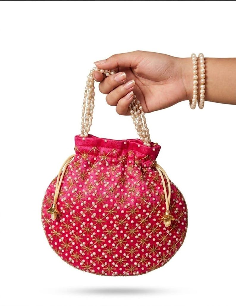 May include: A vibrant hot pink drawstring pouch bag featuring an intricate gold embroidered star pattern and scattered white faux pearls. The bag includes two delicate pearl-beaded handles and light-colored drawstring cords with gold-toned metal ends.