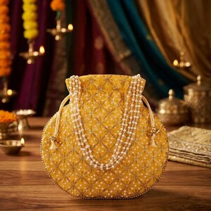 May include: A round yellow drawstring pouch featuring a quilted diamond pattern with gold embroidery and white pearl accents. The bag includes a long, multi-strand pearl handle and matching drawstring cords with small decorative gold-toned metal beads.