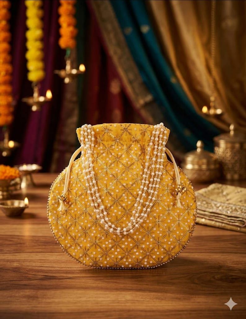 May include: A round yellow drawstring pouch featuring a quilted diamond pattern with gold embroidery and white pearl accents. The bag includes a long, multi-strand pearl handle and matching drawstring cords with small decorative gold-toned metal beads.