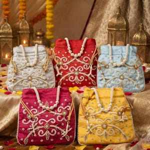 Peut inclure: Cinq pochettes à cordon en argent, rouge, bleu clair, magenta et jaune. Chaque sac présente une broderie dorée complexe, des perles blanches et une anse en perles. Les sacs ont une forme carrée structurée avec des coins arrondis.