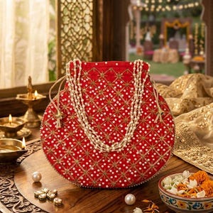 May include: A round red drawstring pouch featuring intricate gold thread embroidery in a diamond pattern, embellished with numerous small white faux pearls. The bag includes a long, multi-strand white faux pearl handle and light-colored cord ties.