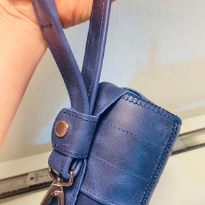 May include: A blue leather bag with a silver clasp and a strap. The bag has a stitched design and a textured surface.