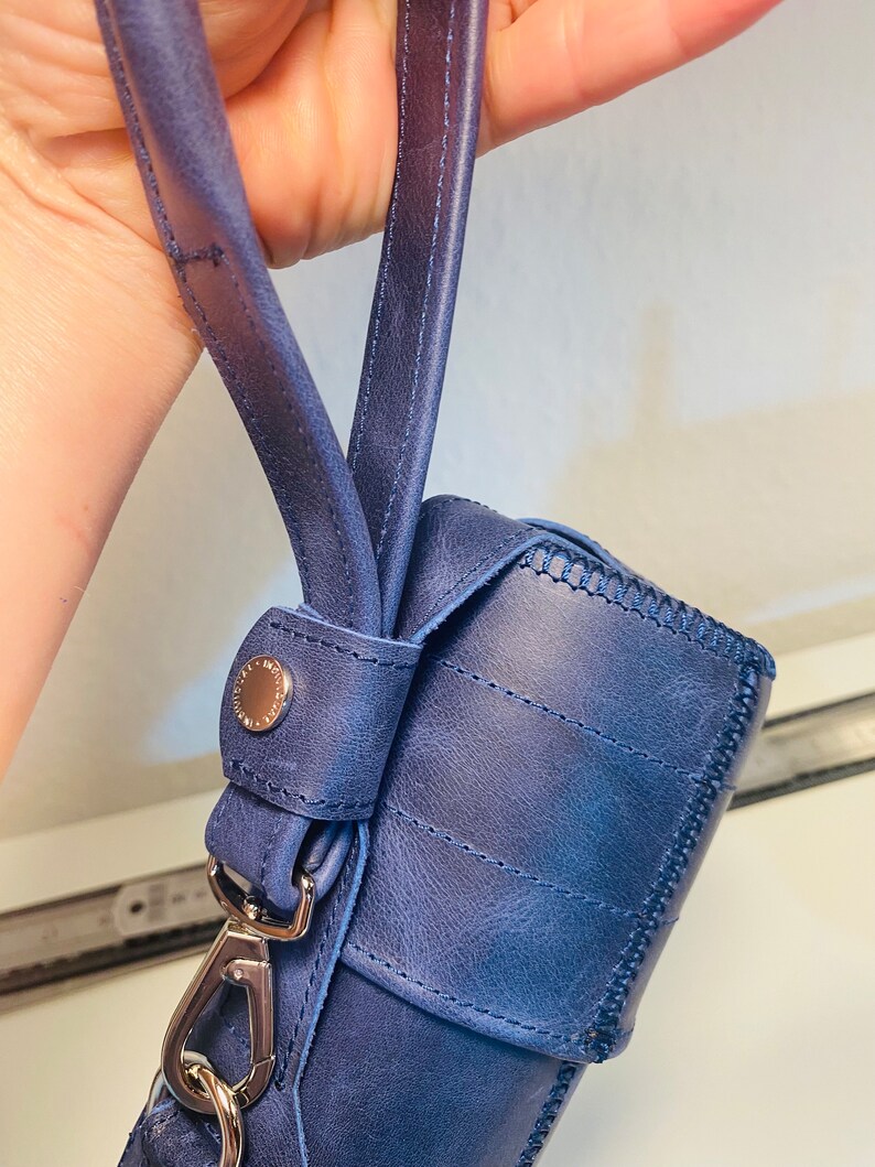 May include: A blue leather bag with a silver clasp and a strap. The bag has a stitched design and a textured surface.