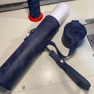 May include: A blue leather roll with a strap and a blue leather round container. A spool of red and blue thread is also in the image.