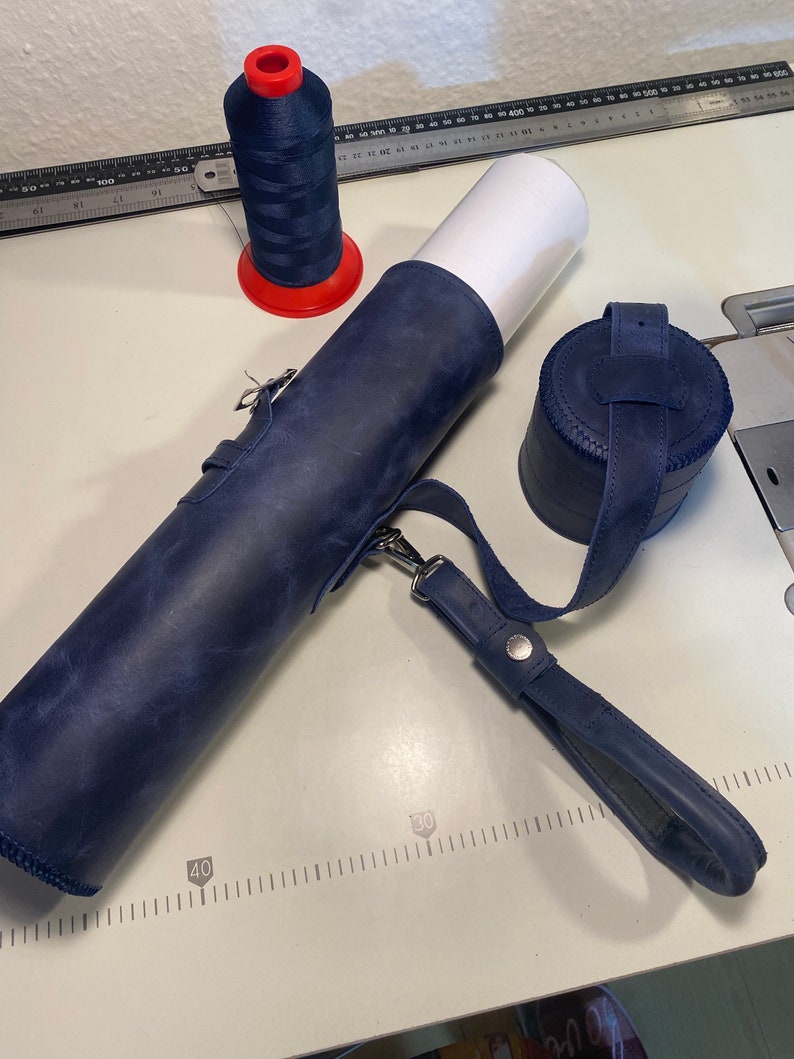 May include: A blue leather roll with a strap and a blue leather round container. A spool of red and blue thread is also in the image.