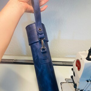 May include: A dark blue leather carrying case with a strap and a silver clasp. The case is cylindrical and has a textured surface.