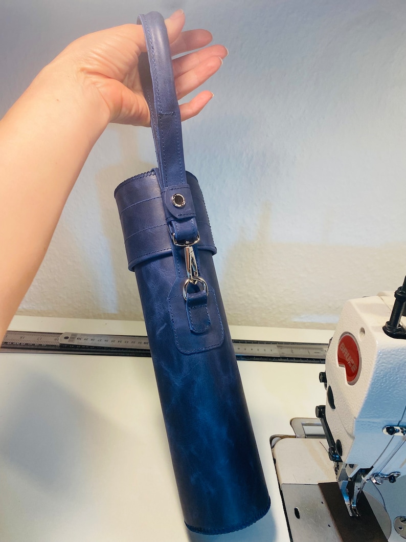 May include: A dark blue leather carrying case with a strap and a silver clasp. The case is cylindrical and has a textured surface.