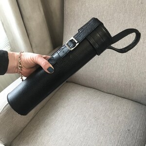 May include: Black leather carrying case with a buckle closure and a strap. The case is rolled up and has a textured surface.