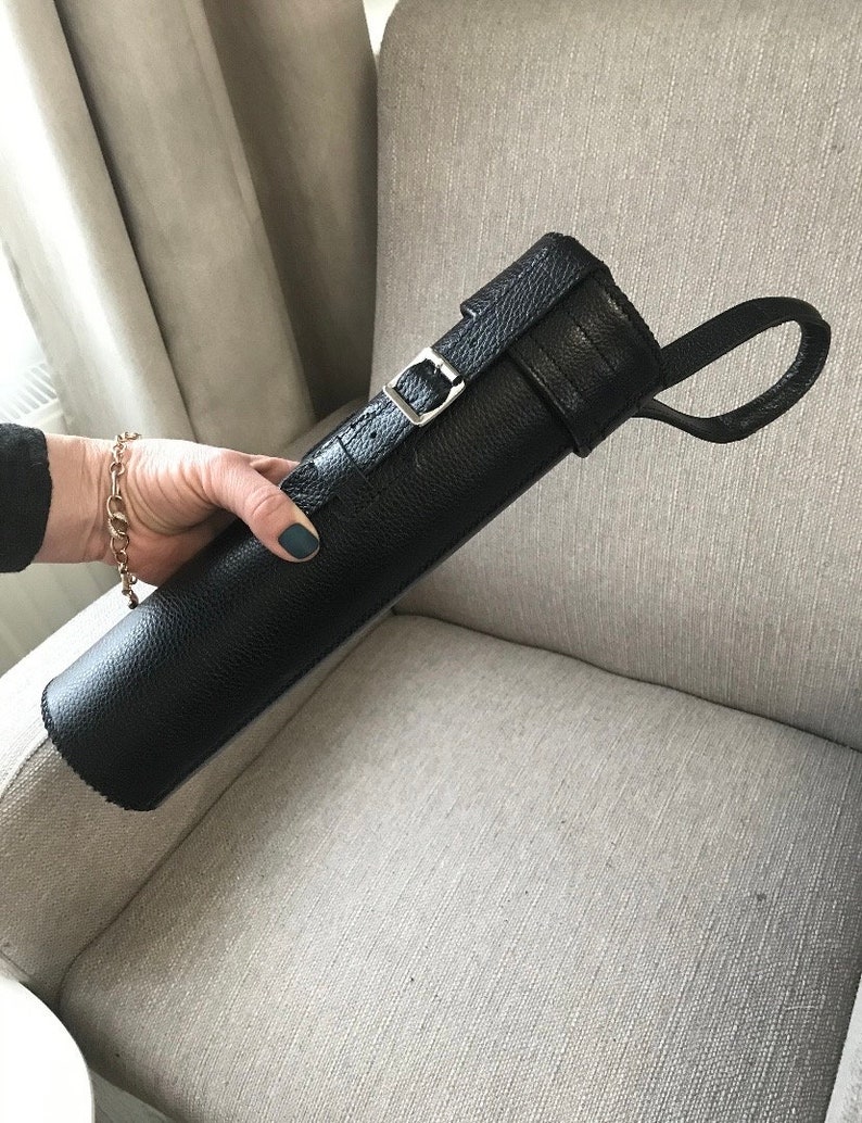 May include: Black leather carrying case with a buckle closure and a strap. The case is rolled up and has a textured surface.