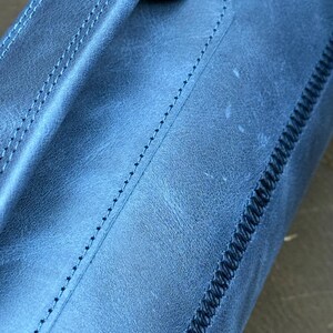 May include: Close-up of a blue leather bag with a stitched handle and a decorative stitch along the edge.