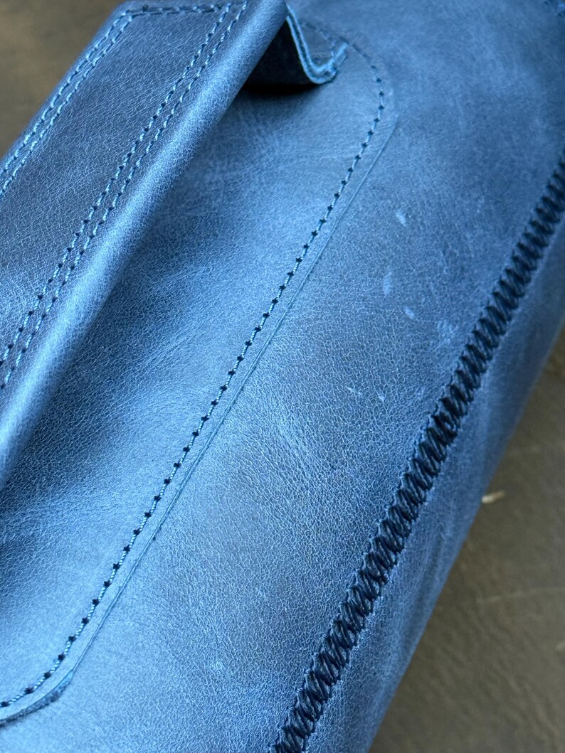 May include: Close-up of a blue leather bag with a stitched handle and a decorative stitch along the edge.