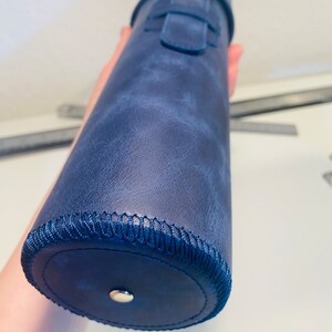 May include: A dark blue leather cylindrical case with a silver buckle and a stitched edge.