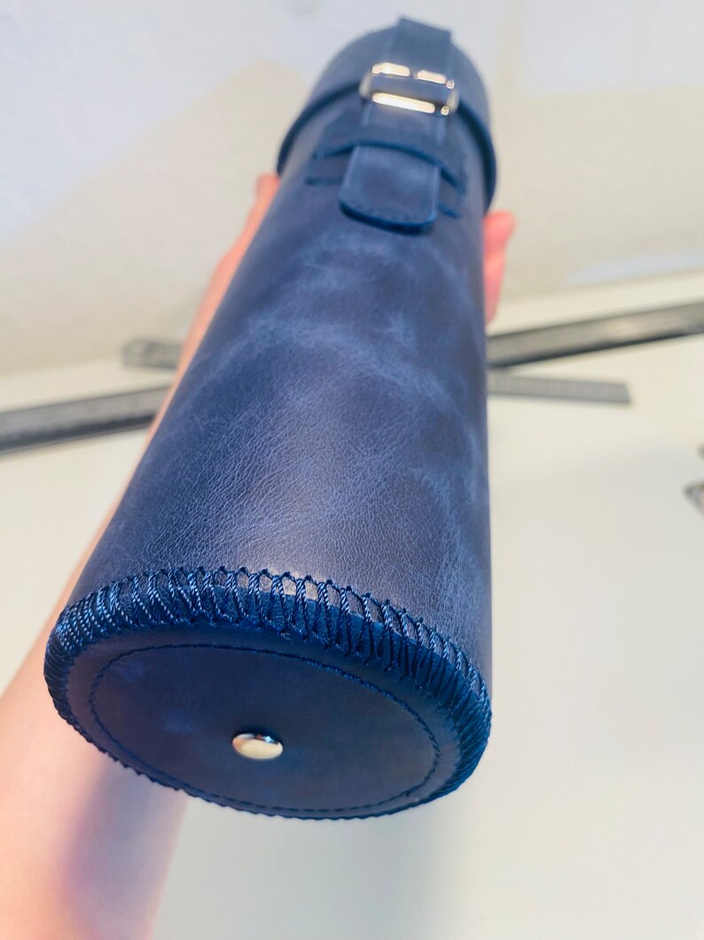 May include: A dark blue leather cylindrical case with a silver buckle and a stitched edge.