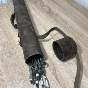 以下が含まれることがあります： ストラップとロールアップデザインのブラウンレザーケース。ケースが開いており、金属製の串がセットになっています。