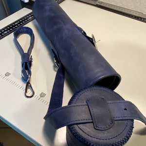 May include: A dark blue leather carrying case with a strap and a round, cylindrical container. The case has a zipper closure and a silver metal clasp.