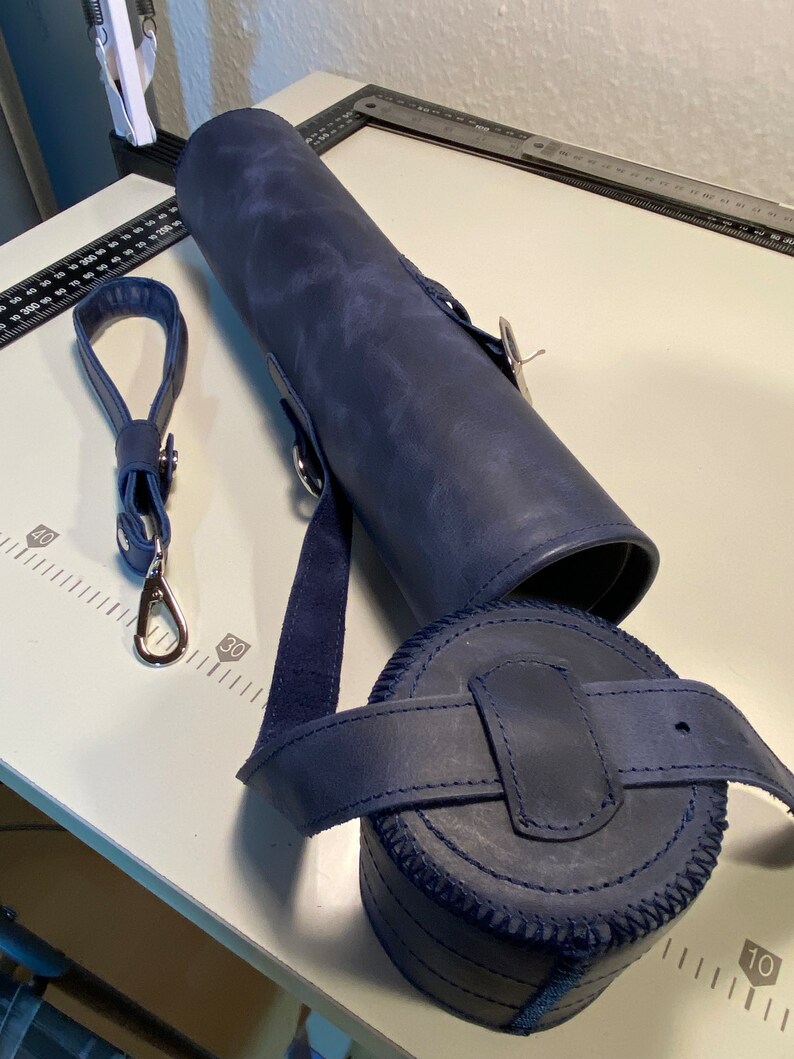 May include: A dark blue leather carrying case with a strap and a round, cylindrical container. The case has a zipper closure and a silver metal clasp.