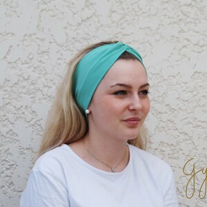 Peut inclure: Un bandeau noué turquoise porté par une personne aux cheveux blonds. Le bandeau est fait d'un tissu doux et extensible.