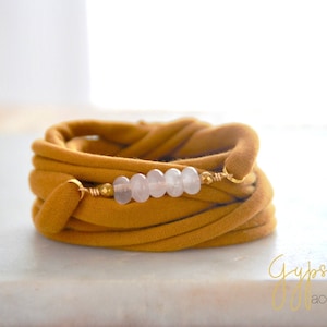 May include: A mustard yellow fabric bracelet with a row of light pink beads and gold accents.