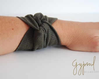 Può includere: Braccialetto verde oliva con superficie strutturata e piccoli puntini neri. Il braccialetto è avvolto attorno a un polso. Il marchio "Gypsoul accessories" è scritto in corsivo.