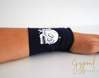 Può includere: Un braccialetto blu navy con un designo di teschio bianco e floreale. Il braccialetto è realizzato in tessuto morbido e confortevole ed è perfetto per aggiungere un tocco di stile a qualsiasi outfit.