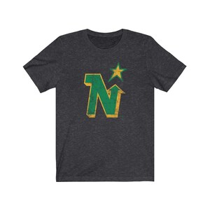 Peut inclure: T-shirt gris fonc&eacute; avec un motif vert et or vieilli. Le motif comprend la lettre "N" avec une fl&egrave;che vers le haut et une &eacute;toile, probablement un logo d'&eacute;quipe. Le t-shirt est en mati&egrave;re souple.
