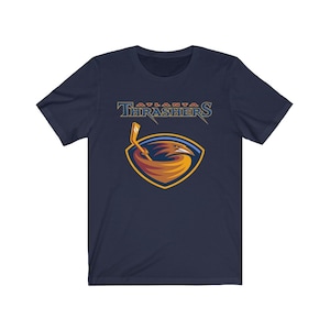 May include: A navy blue t-shirt with the Atlanta Thrashers logo. The logo features a red, orange, and yellow bird with a hockey stick in its beak. The text "Atlanta Thrashers" is above the logo.
