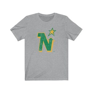 Peut inclure: T-shirt gris chin&eacute; avec un motif vert et or vieilli. Le motif comprend la lettre "N" avec une fl&egrave;che vers le haut, une &eacute;toile et le symbole de la marque. Le t-shirt est fait d'une mati&egrave;re douce et confortable.