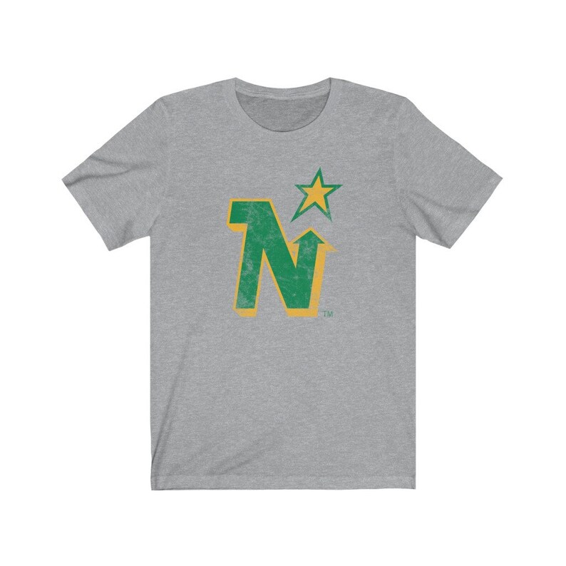 Peut inclure: T-shirt gris chin&eacute; avec un motif vert et or vieilli. Le motif comprend la lettre "N" avec une fl&egrave;che vers le haut, une &eacute;toile et le symbole de la marque. Le t-shirt est fait d'une mati&egrave;re douce et confortable.