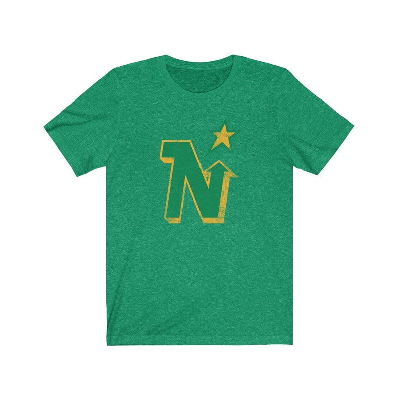 Peut inclure: T-shirt vert avec un motif dor&eacute; vieilli. Le motif repr&eacute;sente la lettre "N" avec une fl&egrave;che vers le haut et une &eacute;toile au-dessus. Le t-shirt est fait d'une mati&egrave;re douce.