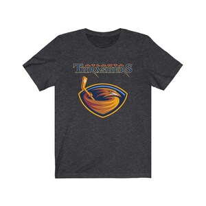 May include: A dark heather grey t-shirt with the Atlanta Thrashers logo. The logo features a red, white, and blue bird with a hockey stick in its beak. The text "Atlanta Thrashers" is above the bird.