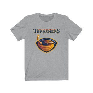 May include: A heather grey t-shirt with the Atlanta Thrashers logo. The logo features a red, orange, and yellow bird with a hockey stick in its beak. The text "Atlanta Thrashers" is above the logo.