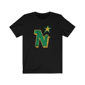 Peut inclure: T-shirt noir avec un motif vert et or vieilli. Le motif comprend la lettre "N" avec une fl&egrave;che vers le haut et une &eacute;toile, probablement pour une &eacute;quipe sportive. Le design a un aspect vintage et us&eacute;.