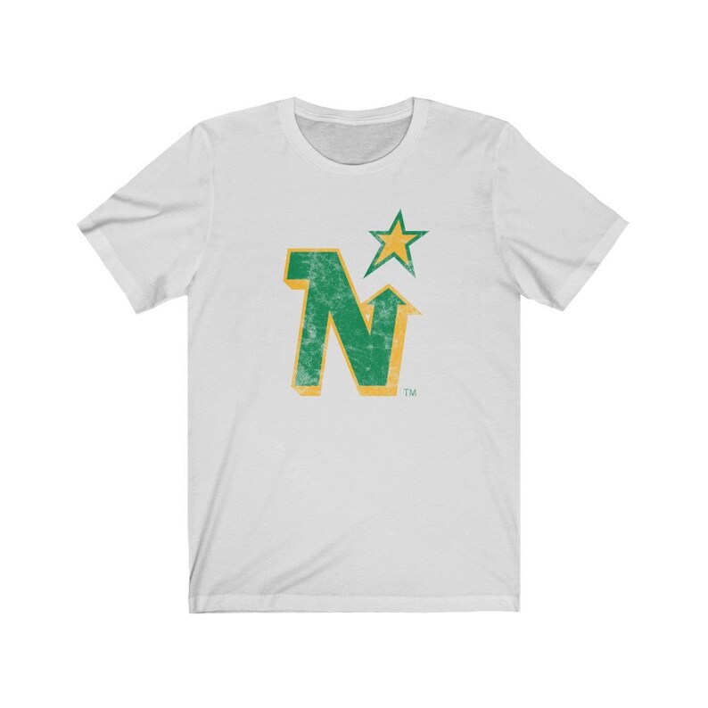 Peut inclure: T-shirt blanc avec un logo vert et dor&eacute; vieilli. Le logo pr&eacute;sente la lettre "N" et une &eacute;toile, avec un aspect vintage. Le t-shirt est &agrave; manches courtes et col rond.