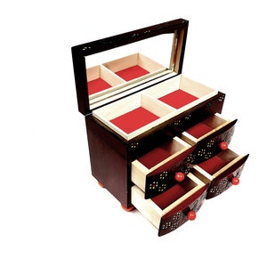 Puede incluir: Una caja de madera para joyas con tapa de espejo y tres cajones. La caja está decorada con un patrón floral y tiene pomos rojos. Los cajones están abiertos, revelando un forro de terciopelo rojo.