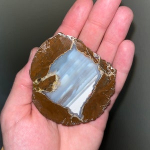 May include: A brown agate geode with a white and blue interior. The geode is about 3 inches in diameter and has a rough, natural texture.