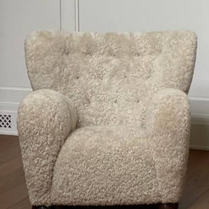 May include: A white sheepskin armchair with a tufted back and rounded arms. The chair has a soft, plush texture and a simple, elegant design.