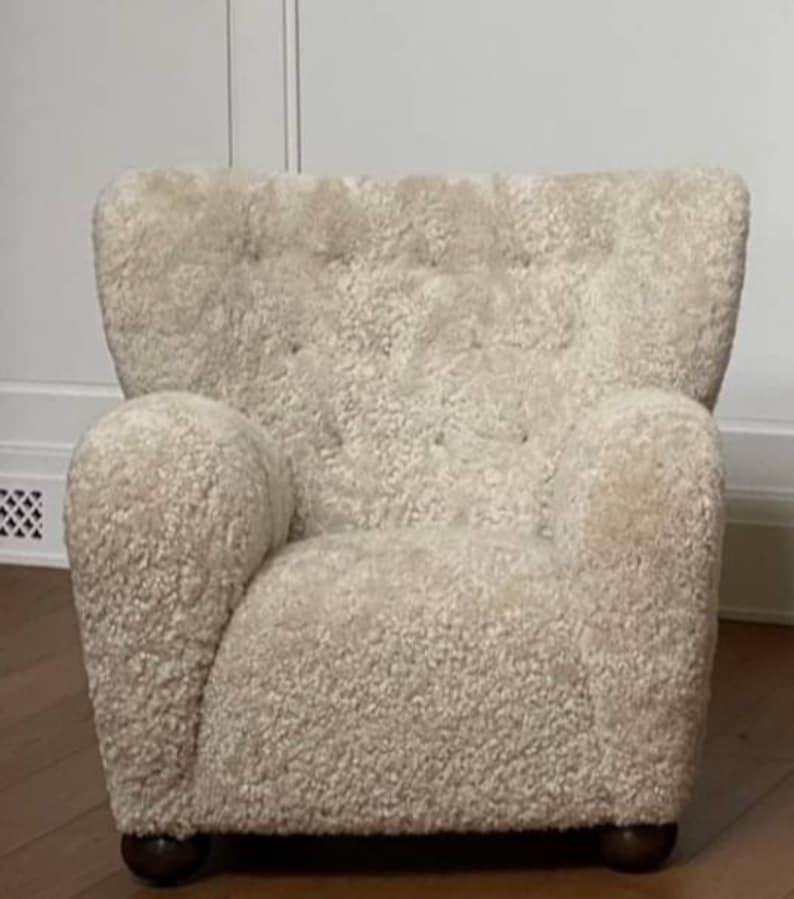 May include: A white sheepskin armchair with a tufted back and rounded arms. The chair has a soft, plush texture and a simple, elegant design.